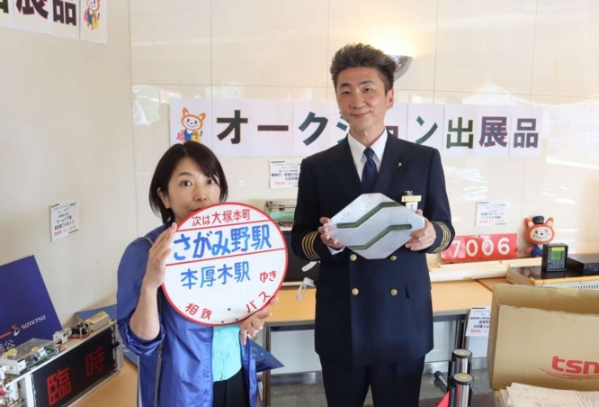バス前面取付 社紋（Sマーク）を持つ小野さんと、バス停留所丸板（本厚木駅行）を持つ山北さん（画像はJタウンネット編集部撮影）