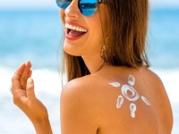 Young woman with sun shape on the shoulder holding sun cream bottle on the beach