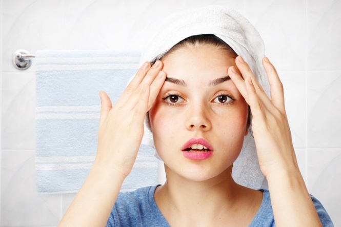 Young girl looking in her bathroom with a towel on her head.