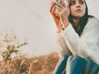 Teenage girl sitting alone on autumn cold day. Lonely sad young woman wearing warm sweater. Loneliness and solitude concept.