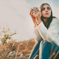 Teenage girl sitting alone on autumn cold day. Lonely sad young woman wearing warm sweater. Loneliness and solitude concept.