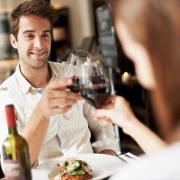 Smiling young man clinking glasses with his girlfriend while at dinner