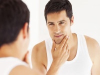 Handsome young man looking himself in the mirror with hand on chin. Horizontal shot.