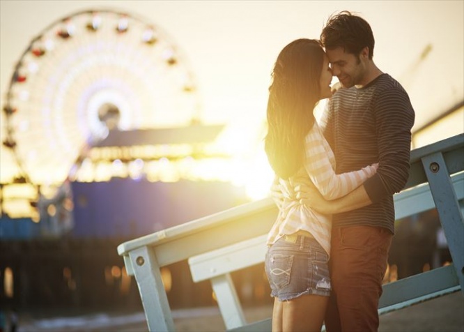 romantic couple kissing at sunset in front of santa monica ferris wheel.