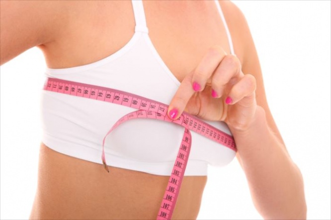 A picture of a young fit happy woman checking her breast measurement over white background
