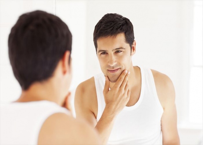 Handsome young man looking himself in the mirror with hand on chin. Horizontal shot.