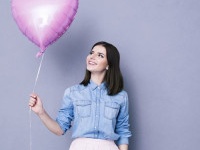 Happy woman holding balloon over gray background. Lookign away.