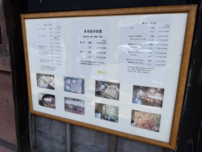 Framed restaurant menu outside a building, with Japanese text and small photos of dishes along bottom.