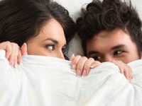 Happy young couple under covers in bed.