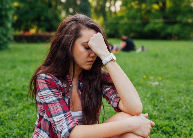 Girl sitting in  the park on the grass. She has headache. What a terrible day