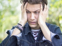 Portrait of frustrated teenage boy against blurred background. Shocked young man standing and holding his head in frustrated position. Blurred background. Horizontal composition. Outdoors shoot. Image edited from Raw format. Young man 18-19 years old. He 