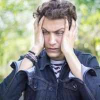Portrait of frustrated teenage boy against blurred background. Shocked young man standing and holding his head in frustrated position. Blurred background. Horizontal composition. Outdoors shoot. Image edited from Raw format. Young man 18-19 years old. He 