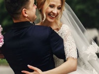 Happy handsome groom and blonde beautiful bride in white dress hugging under arc