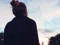 The silhouette of a young woman looking at sunset in the distance.