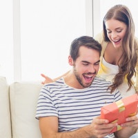 Pretty woman surprising her boyfriend with gift at home in the living room