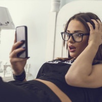 Young woman sitting on bed and reading a shocking text message that she has received.