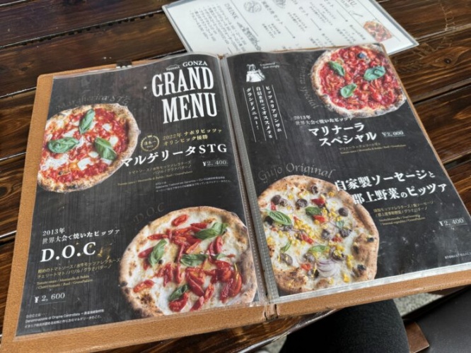 Open menu showing pizzas on black pages with basil leaves and tomato toppings, laid on a wooden table.