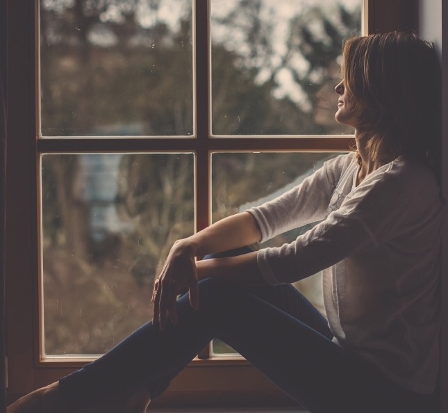 Young attractive woman, sitting on a window, looking outside