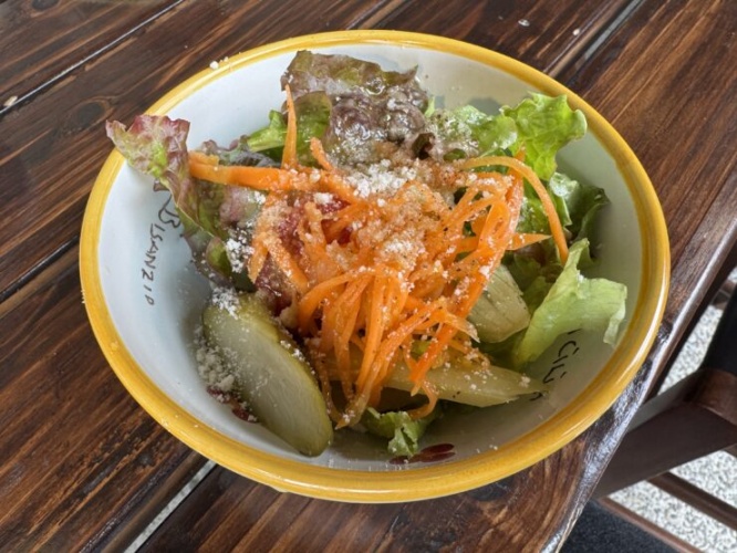 Salad in a yellow-rimmed bowl with lettuce, shredded carrots, and crumbled cheese on a wooden table.