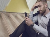 Businessman sitting on a staircase and using mobile phone while having a headache.