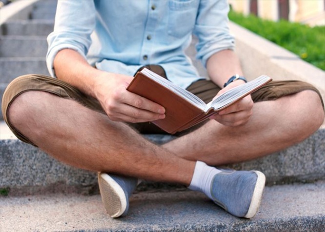 No face. Student with book sit on the stairs in campus.
