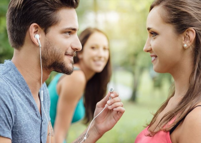 Happy teens relaxing at the park, a guy is sharing his earphones with a girl, they are staring at each other