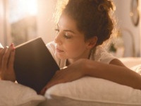 Young woman lying in bed and reading a book.