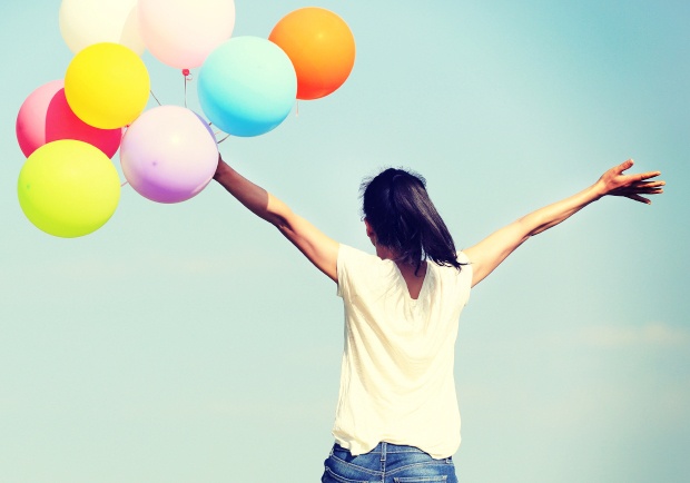 young asian woman running and jumping on green grassland with colored balloons