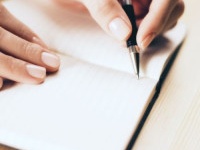 Female hands writing in notebook with pen on wooden table