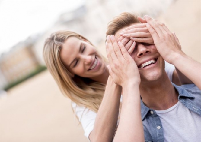 Woman surprising her boyfriend outdoors and covering his eyes - relationship concepts
