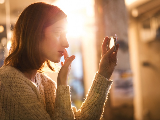 Woman holding hand mirror and fixing make-up.