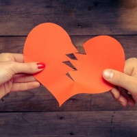 Male and female hands breaks red paper heart, concept of broken love