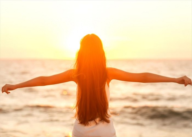 Free woman enjoying freedom feeling happy at beach at sunset. Beautiful serene relaxing woman in pure happiness and elated enjoyment with arms raised outstretched up. Asian Caucasian female model.