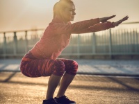 Athletic woman doing squats on a road at sunset.