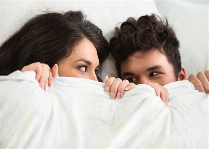 Happy young couple under covers in bed.