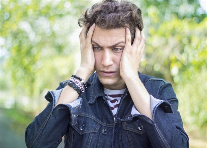 Portrait of frustrated teenage boy against blurred background. Shocked young man standing and holding his head in frustrated position. Blurred background. Horizontal composition. Outdoors shoot. Image edited from Raw format. Young man 18-19 years old. He is wearing a jean jacket. Teenage boy has got short,brown,curly hair. This shocked guy belong to Turkish ethnicity.