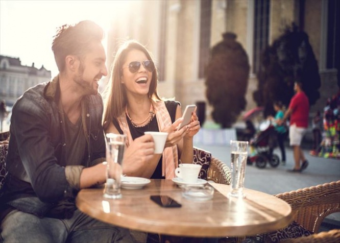 Young happy couple using cell phone while spending a day at a cafe.