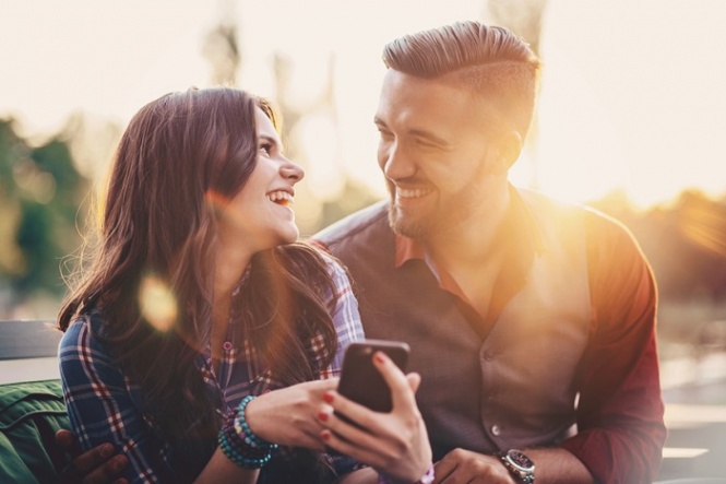 Happy young people with phone texting outdoors