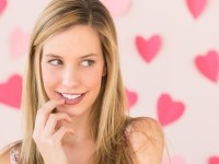 Shy beautiful woman looking away with heart shaped papers stuck against pink background