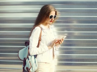 Fashion pretty young woman using smartphone in city over urban g