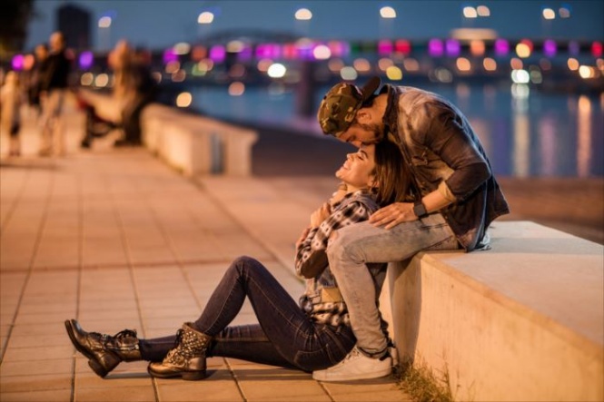 Loving couple relaxing on a riverside during the night while man is kissing his girlfriend on a forehead.