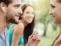 Happy teens relaxing at the park, a guy is sharing his earphones with a girl, they are staring at each other