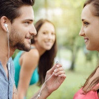 Happy teens relaxing at the park, a guy is sharing his earphones with a girl, they are staring at each other