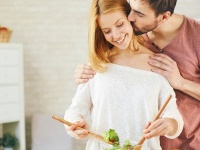 Affectionate young man kissing his wife while she cooking salad