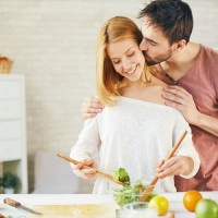 Affectionate young man kissing his wife while she cooking salad