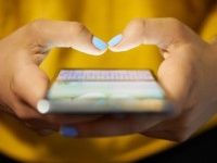 Young woman using cell phone to send text message on social network at night. Closeup of hands with computer laptop in background