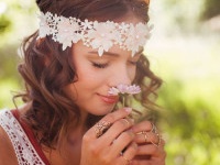 Boho teenager in a sunlit summer park serenely smelling a small pink daisy flower, her eyes closed with pleasure