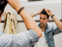 Reflection of Young Man Bushing Hair in Mirror Getting Ready to Go Out