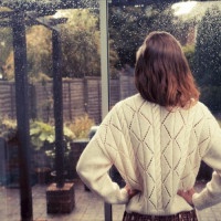 A young woman is standing by the french doors in her house and is looking out at the rain