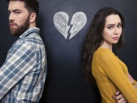 Unhappy young couple standing with arms crossed over background of chalkboard with drawn broken heart